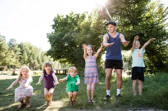 Kindergruppe mit Betreuer springend auf einer Wiese