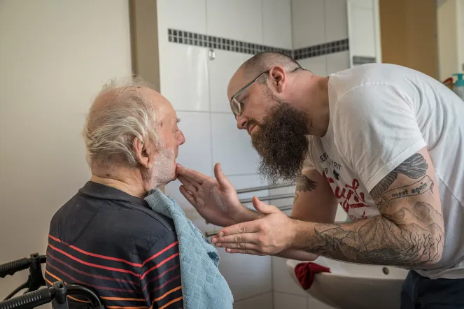 Eine Pflegekraft unterstützt einen Bewohner in einer Wohngruppe bei der Körperpflege.